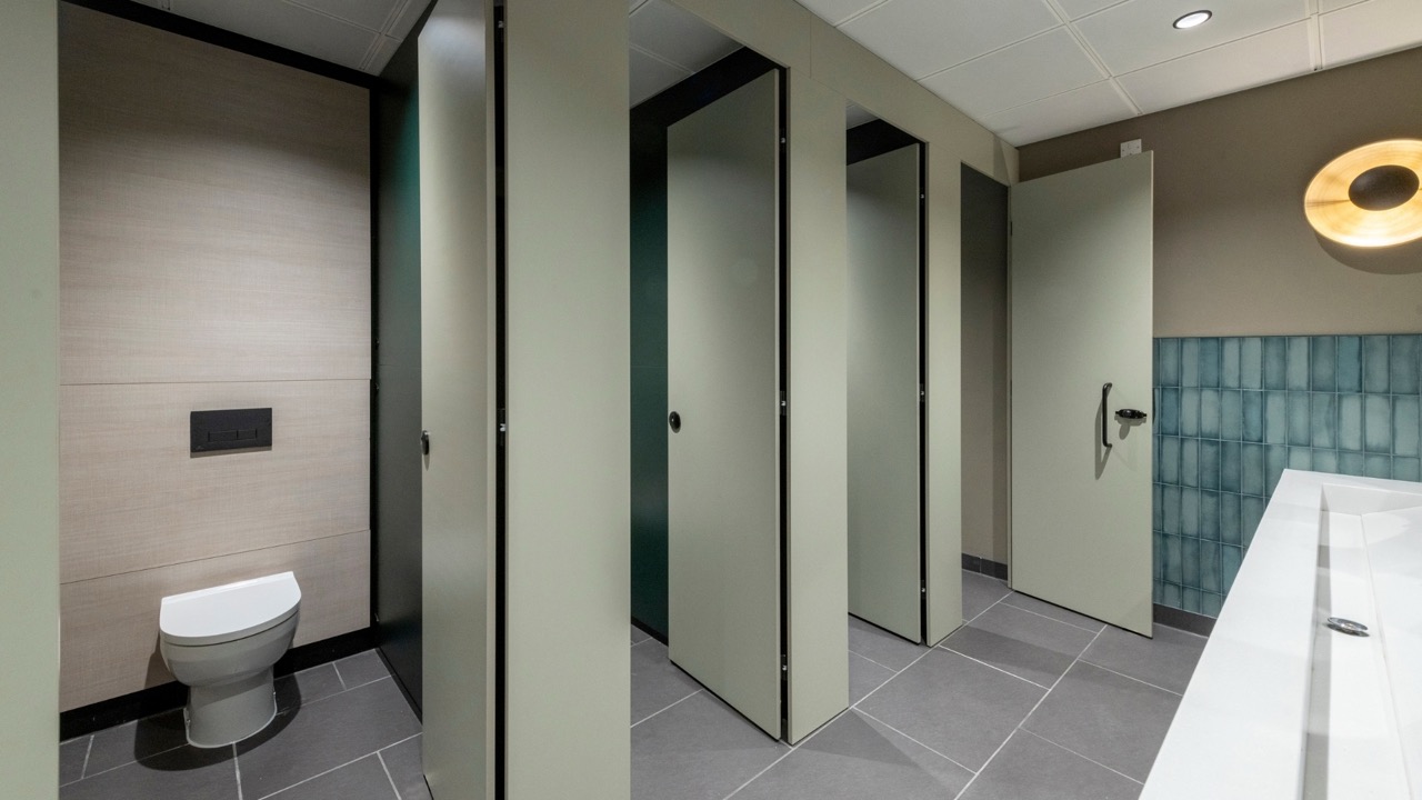 Row of flush Identity washroom cubicles with doors open. Opposite features a solid surface wash trough. 