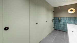A row of flush fronted Identity washroom cubicles next to a solid surface wash trough vanity