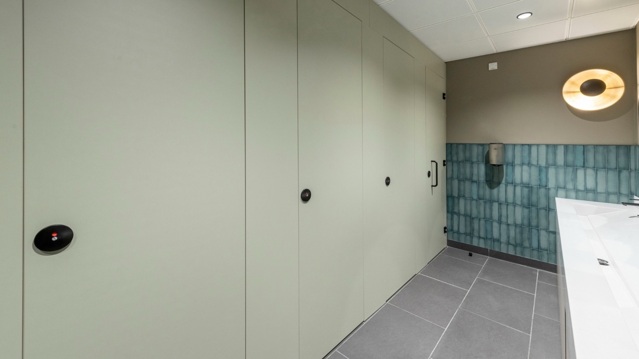 A row of flush fronted Identity washroom cubicles next to a solid surface wash trough vanity